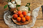 Apricots (Prunus armeniaca) and candle in a wooden plate on a flowery table in the countryside with old lace to embellish the table
