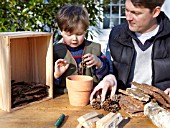 INSECT HOUSE BUILDING PROJECT WITH FATHER AND SON.  PLACING CONES IN POT.  STEP 8
