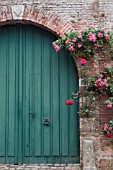 BLUE ARCHED DOOR IN BRICK GATEWAY WITH RED AND PINK CLIMBING ROSES