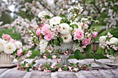MALUS X EVERESTE WITH OUTDOOR TABLE SET UNDER APPLE BLOSSOMS AND DECORATED WITH FLORAL ARRANGEMENTS OF RANUNCULUS AND ROSES