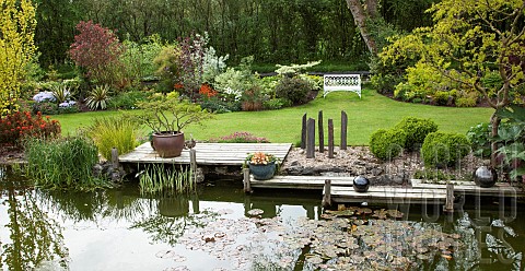 Pond_with_decking_silver_ornate_balls_grey_slate_pillars_borders_of_colourful_mature_shrubs_and_tree