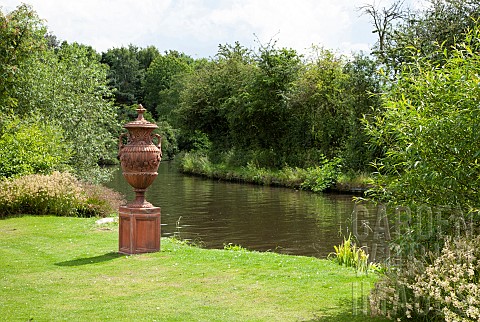 Mature_trees_on_edge_of_canal_large_ornate_terra_cotta_urn_on_plinth_in_June_Early_Summer
