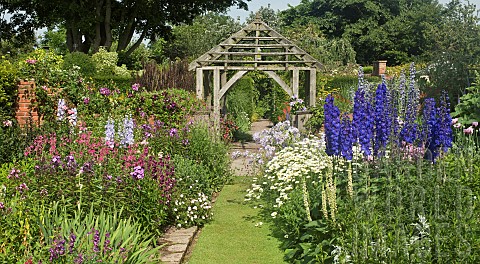 Deep_borders_of_mixed_colours_and_varieties_of_herbaceous_perennials_grass_path_leading_to_oak_pergo