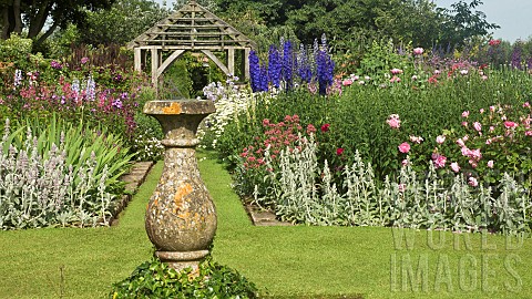 Stone_sundial_in_lawn_with_twin_borders_of_many_colours_and_varieties_of_herbaceous_perrenials